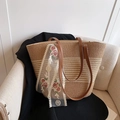 Primer plano del bolso tote de paja con asas de cuero marrón y detalle de pañuelo de encaje - Caqui