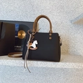 Close-up of black crossbody bag with brown round handle and wooden horse charm detail - Black With Pendant