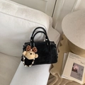 Close-up of black Boston bag on white sofa featuring an embossed logo and cute bear charm - Black (With Charm)