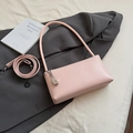 Detailed view of pink leather baguette bag with silver bean charm on a gray suit background - Pink With Pendant