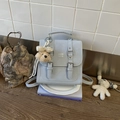 Close-up of a light blue square bag with metal buckles and a cute teddy bear charm - Blue