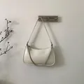 Detalle de bolso bandolera blanco crema con cadena de plata y logo NO FILTER en pared neutra - Blanco Roto