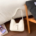 Detailed view of a vintage cream hobo bag with a decorative metal buckle on a wooden floor - White