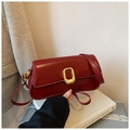 Detail of a deep red rectangular shoulder bag with golden metallic buckle on a white book - Red
