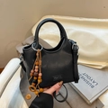 Detalle de bolso tipo cubo de cuero negro con colgante de madera y placa metálica de marca - Negro