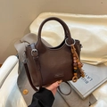 Detalle de bolso tipo cubo en cuero marrón oscuro con textura lichi y colgante de madera - Marrón
