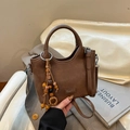 Detalle de un bolso cubo marrón con colgante de cuentas de madera boho y correa ajustable - Marrón