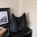 Detail view of large black nylon tote bag with functional pockets on a glossy surface - Black