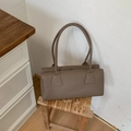 Bolso baguette beige minimalista en un taburete tejido contra una pared blanca - Marrón