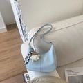 Dettaglio borsa a mezzaluna azzurra con ciondolo di peluche su un divano bianco - Con Ciondolo / Blu
