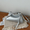 Detail der silbernen Metallic-Tasche mit Falten-Design und Goldschnalle auf Holzfläche - Silber