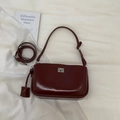 Close-up of a burgundy glossy leather baguette bag with silver buckle and adjustable strap - Red