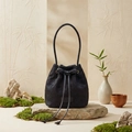 Detail of black woven bucket bag with floral texture and drawstring on stone pedestal - Black