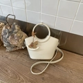 Detail der cremeweißen Leder-Eimertasche mit Holzpferd-Anhänger und feinen Nähten - Gebrochenes Weiß