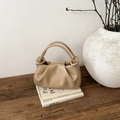Dettaglio della borsa a mano a nuvola plissettata in pelle beige su base in legno - Cachi