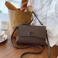 Detail of dark brown fabric crossbody bag with M-shaped metal buckle on a wooden table - Brown