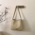 Detail der cremefarbenen Ledertasche mit elegantem Gold-Logo und hochwertigen Beschlägen - Gebrochenes Weiß