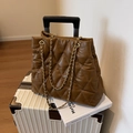 Brown quilted tote bag with gold chain strap on a white suitcase in a travel setting - Coffee