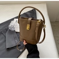 Coffee brown retro leather bucket bag with gold clasp held against a suit backdrop - Tan