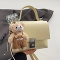 Elegant beige square handbag with silver clasp and cute bear charm held by hand - Light Yellow + Khaki Bear
