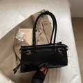 Glossy black vintage underarm bag with gold buckles on white fabric background - Black