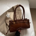 Retro deep brown faux leather shoulder bag with gold buckle on a white bed - Brown