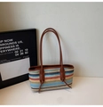 Macro shot of colorful woven tote bag featuring brown leather trim and protective metal feet - Colorful