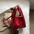Bolso cubo rojo vintage con textura de cocodrilo, asas dobles y correa ajustable sobre cama - Burdeos
