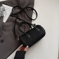 Chic black pleated cylindrical crossbody bag displayed on a dark grey suit jacket - Black