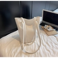 Detailaufnahme der weißen Eimertasche mit Krokodilmuster und dünnen Riemen auf Bettwäsche - Gebrochenes Weiß