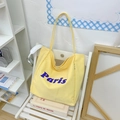Detalle de un bolso tote de lona amarilla con estampado Paris morado en silla blanca - Amarillo