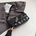 Glossy black underarm bag with silver eyelets and adjustable strap on a grey blazer - Black