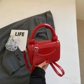 Detalle de bolso cuadrado en charol rojo brillante con asa cilíndrica y correa ajustable - Rojo