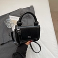 Detail of minimalist black leather crossbody bag with unique round handle and silver lettering - Black