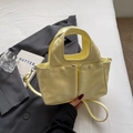 Dettaglio della borsa gialla che mostra le tasche frontali e il manico integrato - Giallo
