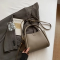 Taupe pebbled leather bucket bag with top handle and bear charm on a grey suit - Gray