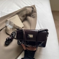 Macro shot of dark brown glossy leather shoulder bag with silver chain and metal nameplate - Coffee