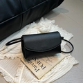 Détail d'un petit sac bandoulière en cuir noir avec rabat posé sur un livre français - Noir