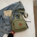 Close-up of a light green nylon mini crossbody bag featuring a round logo on white bedding - Green