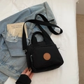 Detail view of black nylon crossbody bag with leather logo and wide fabric strap - Black