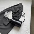 Schicke schwarze Zylindertasche aus glänzendem Leder auf einem grauen Sakko - Schwarz ohne Anhänger
