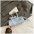 Détail d'un sac à main bleu clair verni avec nœuds en dentelle et pendentif étoile argenté - Bleu