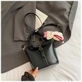 Glossy black bucket bag with gold hardware and a cute plush bear charm on a suit - Black