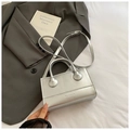 Detalle del bolso de cuero plateado con letras grabadas sobre fondo de chaqueta gris - Plateado