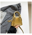 Detailed view of mini metallic shell bag featuring glossy texture and top handle - Gold