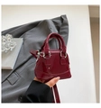 Detailed close-up of a mini dark red patent leather shell bag held in hand by a person - Red