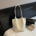 Close-up of off-white crocodile embossed tote bag with slim shoulder straps on a white bed - White