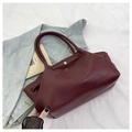 Chic burgundy leather tote bag with slim handles and gold hardware in a fashion setting - Red