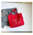 Dettaglio di una borsa tote in tela rossa con scritte bianche su una scrivania elegante - Rosso