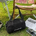 Minimalist black cylinder sports crossbody bag with white lettering on green grass - Black